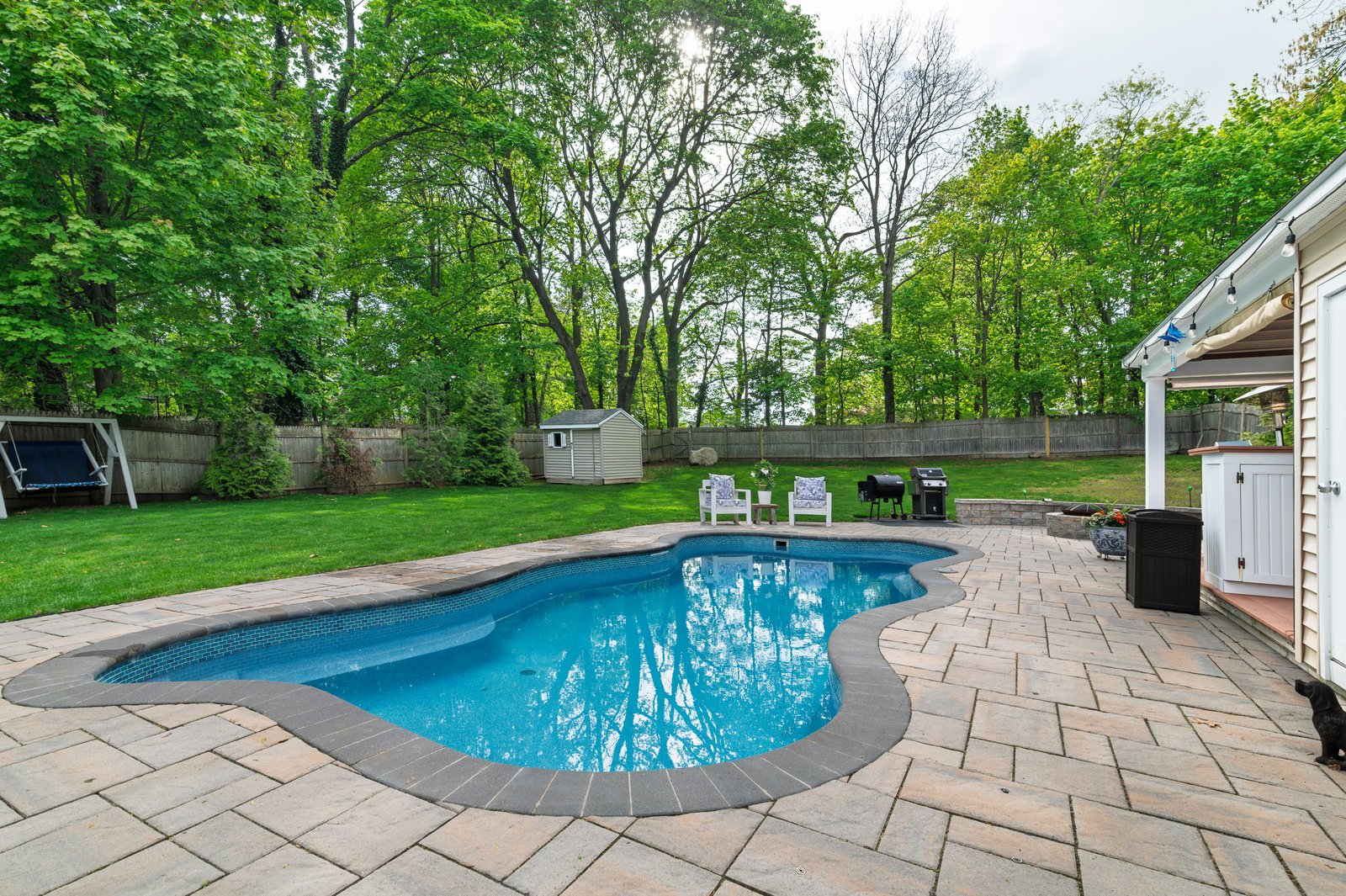 Heated saltwater fiberglass pool at twilight with the covered pavilion lit in the background at 51 Faxon Street, Braintree MA